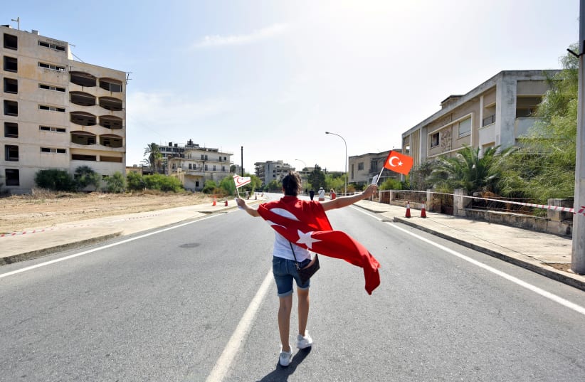 A woman walks while holding Turkish and Turkish Cypriot flags inside an area fenced off by the Turkish military since 1974, in the abandoned coastal area of Varosha, a suburb of the town of Famagusta in Turkish-controlled northern Cyprus, October 8, 2020. (photo credit: REUTERS/HARUN UCAR)