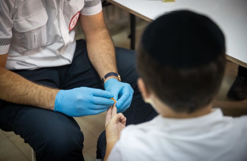  A Magen David Adom (MDA) worker taking a serological tests for COVID-19 from an ultra-Orthodox child in the ultra-Orthodox town of Kiryat Ye’arim (Telz-Stone), outside Jerusalem, August 9, 2021. (photo credit: YONATAN SINDEL/FLASH90)