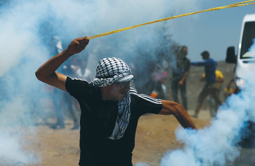   A PALESTINIAN DEMONSTRATOR uses a slingshot during a protest against settlements. (photo credit: MOHAMAD TOROKMAN/REUTERS)