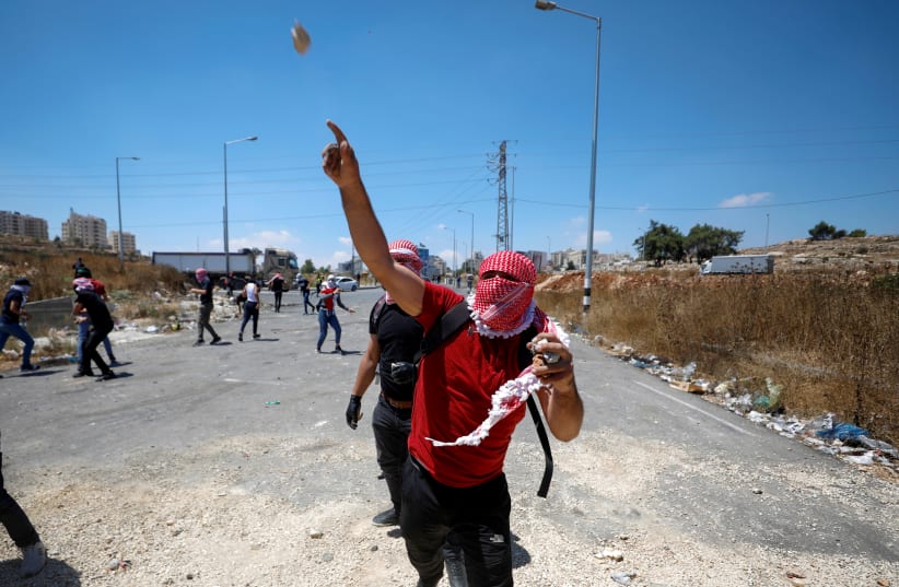  A Palestinian demonstrator hurls a stone at Israeli forces during a protest over the killing of four Palestinians by Israeli forces in a clash, near Israeli settlement of Beit El in the Israeli-occupied West Bank August 17, 2021 (photo credit: MOHAMAD TOROKMAN/REUTERS)