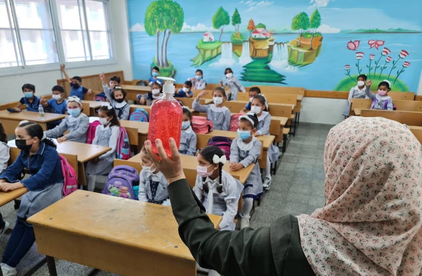  A teacher talks to her students about the importance of hand-washing with hand sanitizer on the first day of the new school year in the Gaza Strip, August 16, 2021. (photo credit: HASSAN ESLIEH/THE MEDIA LINE)