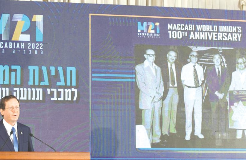  PRESIDENT ISAAC HERZOG at the Maccabi World Union centenary celebration, with a background photograph in which his father is pictured in the group photo taken at the 12th Maccabiah Games.  (photo credit: AMOS BEN-GERSHOM/GPO)