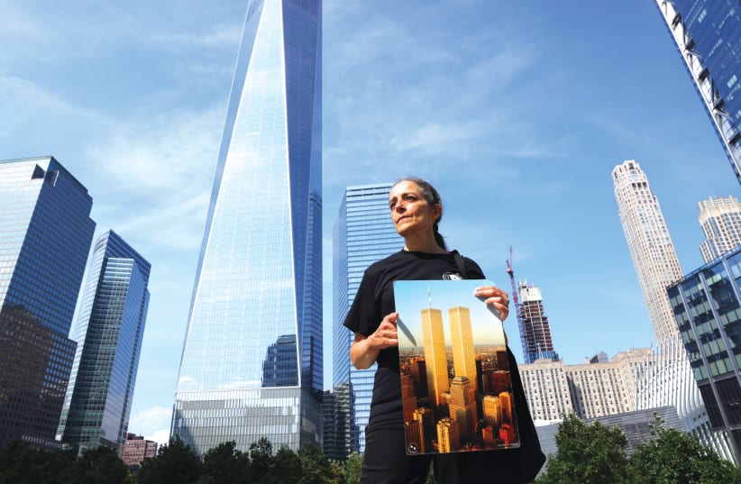  JOAN MASTROPAOLO, a docent at the 9/11 Tribute Museum, holds an archival photograph of the Twin Towers in front of One World Trade Center in New York. (photo credit: CAITLIN OCHS/REUTERS)