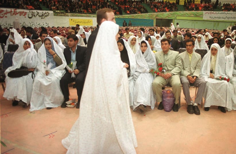 A just-married Iranian couple walks past other couples attending a mass wedding celebration at Azadi Sport Centre in Tehran February 27, 2002 where about 900 people tied the knot. (photo credit: REUTERS/Nikoubazl CJF/GB)