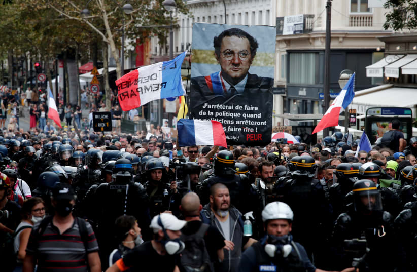  Demonstrators hold up a banner with an image of late French humorist Coluche during a protest against France's restrictions, including compulsory health passes, to fight the coronavirus disease (COVID-19) pandemic, in Paris, France, September 11, 2021. (photo credit: REUTERS)