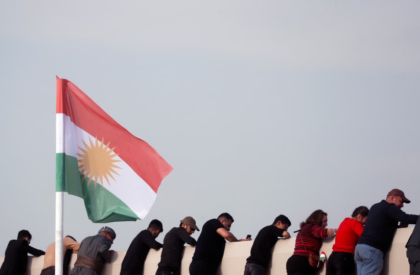  People stand next to a Kurdistan flag as they wait for Pope Francis to hold a mass at Franso Hariri Stadium in Erbil, Iraq, March 7, 2021. (photo credit: REUTERS/YARA NARDI)