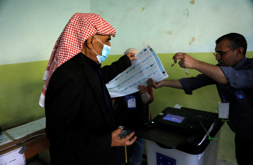 A voter hands a ballot paper to a poll worker at a polling station, as Iraqis go to the polls to vote in the parliamentary election, in Mosul, Iraq October 10, 2021. (photo credit: REUTERS/KHALED AL-MOUSILY)
