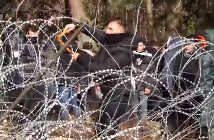 Migrants use wire cutters to cut the barbed wire as they try to cross the Belarus/Poland border near Kuznica Bialostocka, Poland, in this video-grab released by the Polish Defence Ministry, November 8, 2021. (photo credit: MON/HANDOUT VIA REUTERS)