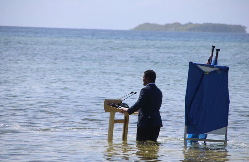Tuvalu's Minister for Justice, Communication & Foreign Affairs Simon Kofe gives a COP26 statement while standing in the ocean in Funafuti, Tuvalu November 5, 2021. (photo credit: Courtesy Tuvalu's Ministry of Justice, Communication and Foreign Affairs / Social Media via REUTERS)