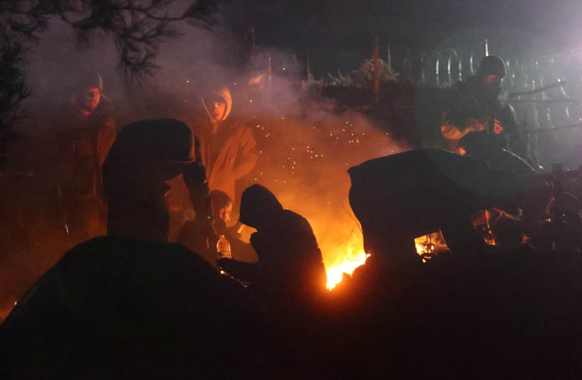 Migrants gather around a fire near a barbed wire fence in a makeshift camp on the Belarusian-Polish border in the Grodno region, Belarus November 11, 2021. Picture taken November 11, 2021. (photo credit: Ramil Nasibulin/BelTA/Handout via REUTERS)