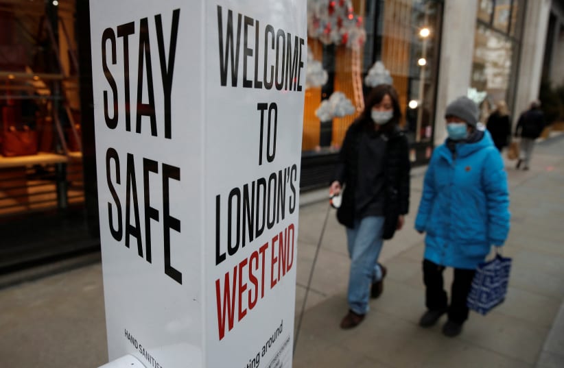  Shoppers walk past a coronavirus related warning sign, amid the coronavirus disease (COVID-19) pandemic in London, Britain, December 11, 2021. (photo credit: REUTERS/PETER NICHOLLS)