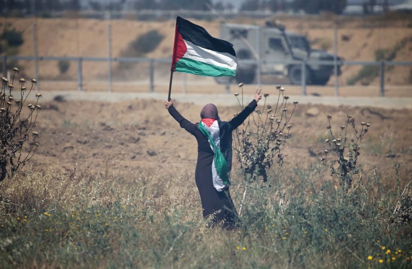 A woman holds a Palestinian flag during a protest marking the 71st anniversary of the ‘Nakba’ at the Israel-Gaza border fence in 2019. (photo credit: IBRAHEEM ABU MUSTAFA/REUTERS)