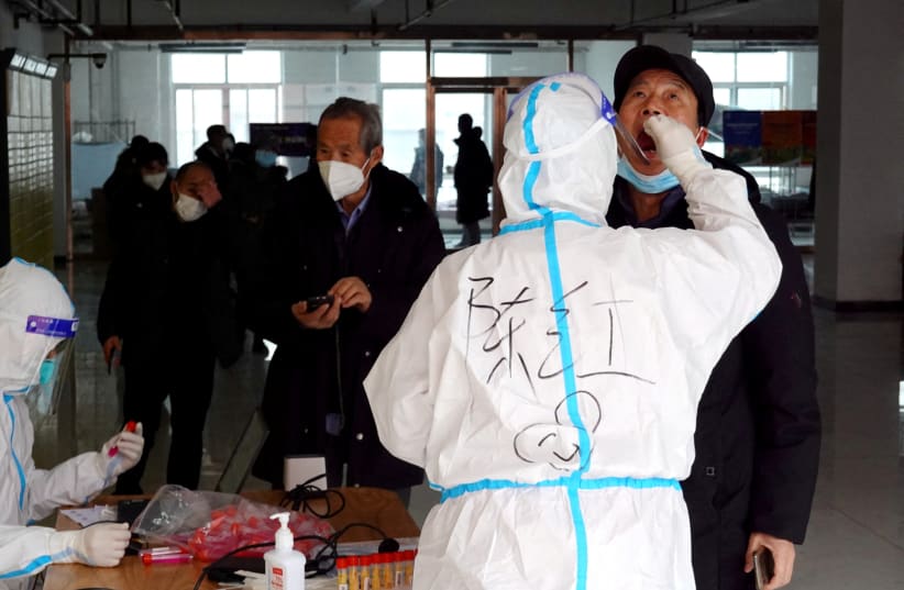 A medical worker in protective suit collects a swab sample from a man for nucleic acid testing at a residential compound, during another round of mass testing following the coronavirus disease (COVID-19) outbreak in Xian, Shaanxi province, China, December 27, 2021. (photo credit: CNSPHOTO VIA REUTERS)