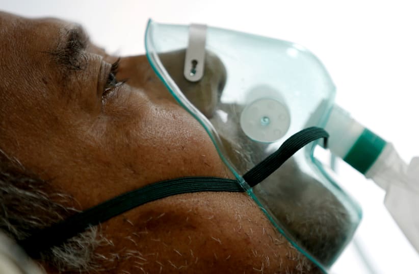 A patient suffering from the coronavirus disease (COVID-19) breathes with a non-rebreather mask in an isolation room at a hospital in Bogor, Indonesia, January 26, 2021. (photo credit: REUTERS/WILLY KURNIAWAN/FILE PHOTO)