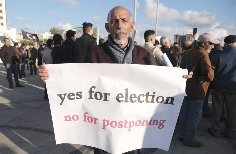  A MAN holds a banner during a protest in Benghazi against the delay in holding the Libyan presidential election initially planned for December 24. (photo credit: ESAM OMRAN AL-FETORI/REUTERS)
