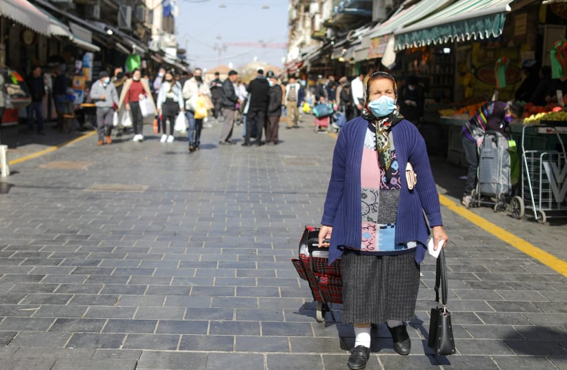  An Israeli woman wearing masks is seen walking in Jerusalem's Machane Yehuda market on January 13, 2022 (photo credit: MARC ISRAEL SELLEM/THE JERUSALEM POST)
