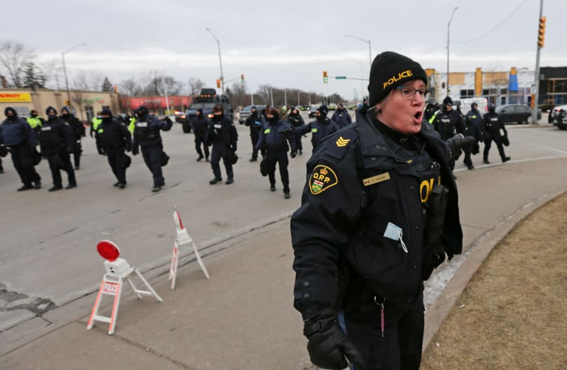  A police officer reacts on the road leading to the Ambassador Bridge, which connects Detroit and Windsor, after police cleared demonstrators, during a protest against coronavirus disease (COVID-19) vaccine mandates, in Windsor, Ontario, Canada February 13, 2022.  (photo credit: REUTERS/CARLOS OSORIO)