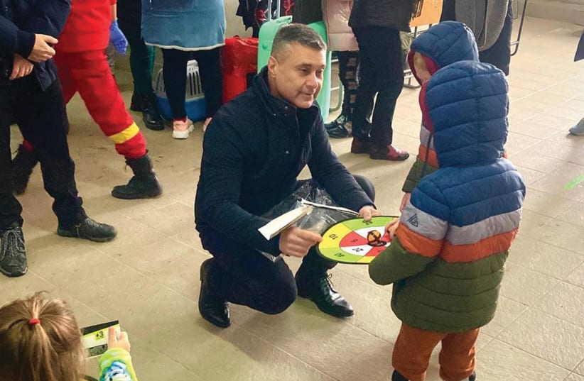  ISRAEL’S AMBASSADOR to Romania, David Saranga, shows a game to children at a refugee center set up at the Ukraine-Romania border. (photo credit: Israel Embassy in Romania)