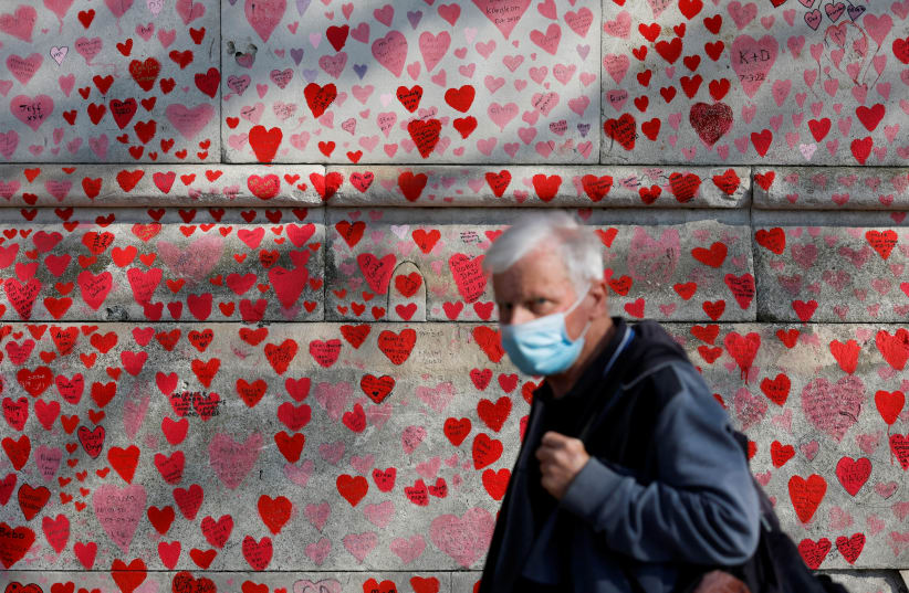  A man wearing a face-mask walks past The National Covid Memorial Wall, on national day of reflection to mark the two year anniversary of the UK going into national lockdown, in London (photo credit: REUTERS/PETER CZIBORRA)