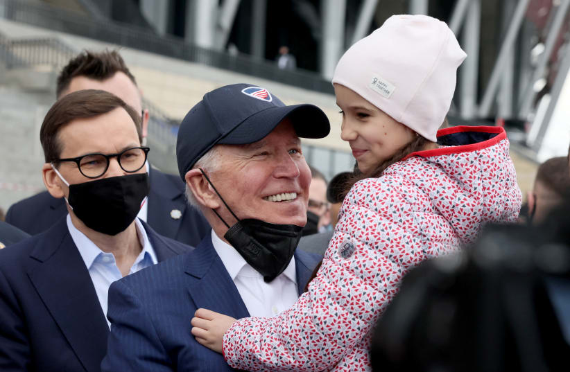 US President Joe Biden, flanked by Polish Prime MInister Mateusz Morawiecki, holds a child as he visits Ukrainian refugees at the PGE National Stadium, in Warsaw, Poland March 26, 2022.  (photo credit: REUTERS/EVELYN HOCKSTEIN)