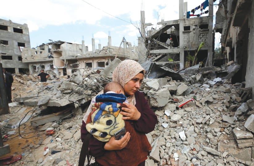  A PALESTINIAN WOMAN carries her child amid the rubble during the Israel-Hamas fighting in Gaza last May. Does ‘The New York Times’ publish front-page photo galleries of child victims of the Russian aggression, as it did with last year’s Gaza war? (photo credit: MOHAMMED SALEM/REUTERS)