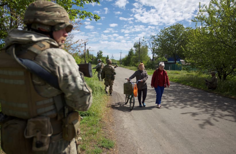 Local women walk along a street while Ukrainian servicemen patrol an area, as Russia's attack on Ukraine continues, in the town of Kurakhove, in Donetsk region, Ukraine, May 20, 2022. (photo credit: REUTERS/ANNA KUDRIAVTSEVA)