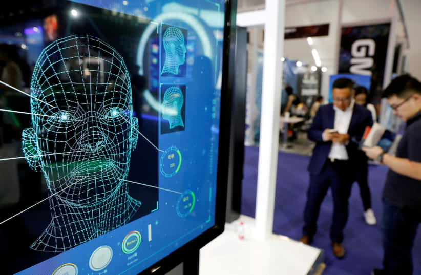  Visitors check their phones behind the screen advertising facial recognition software during Global Mobile Internet Conference (GMIC) at the National Convention in Beijing (photo credit: REUTERS)