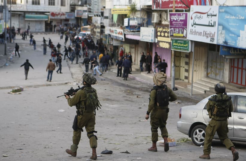  ISRAELI SOLDIERS walk with their weapons behind a group of Palestinians during clashes in Hebron in 2012. Korn questions what Judaism says about how the IDF should conduct itself. (photo credit: MUSSA QAWASMA/REUTERS)