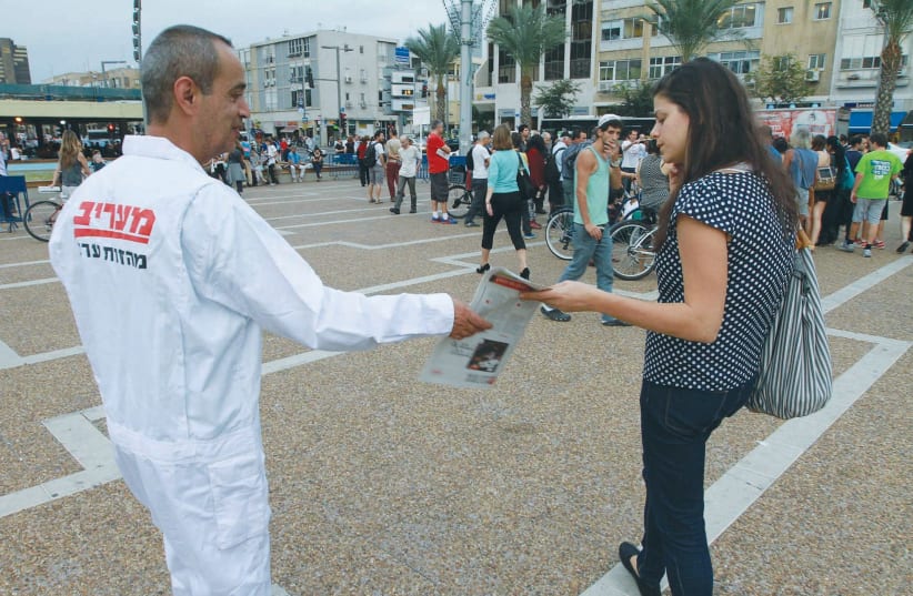  A MAN HANDS out  the ‘Maariv’ newspaper in Tel Aviv’s Rabin Square.   (photo credit: Illustrative file photo: Eli Dassa/Maariv)