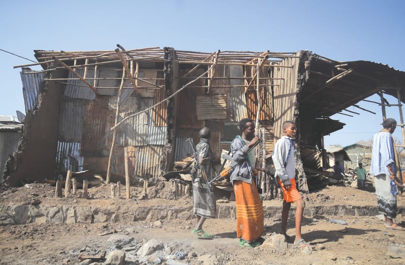  RESIDENTS AND militias stand next to houses destroyed by an air strike during the fight between the Ethiopian National Defense Forces and Tigray People’s Liberation Front in Afar region, Ethiopia, earlier this year.  (photo credit: TIKSA NEGERI / REUTERS)