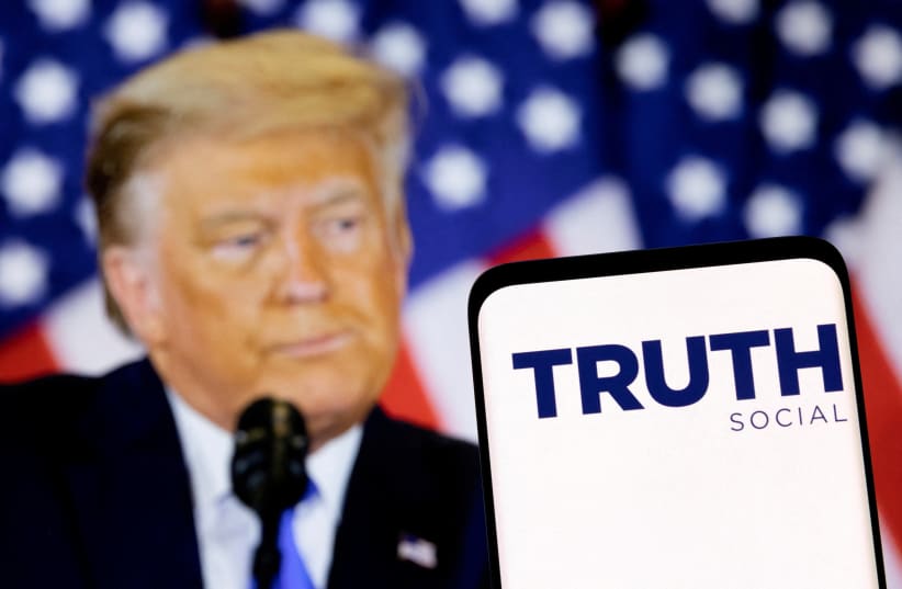  The Truth social network logo is seen on a smartphone in front of a display of former U.S. President Donald Trump in this picture illustration taken February 21, 2022.  (photo credit: DADO RUVIC/REUTERS)