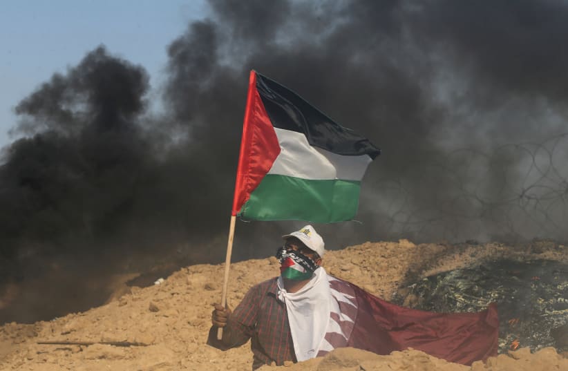  A protester wears a Qatar flag and waves a Palestinian flag during clashes with Israeli troops near the border between Israel and Central Gaza Strip July 7, 2017 (photo credit: IBRAHEEM ABU MUSTAFA/REUTERS)