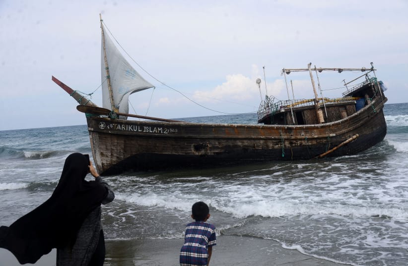  Locals stand near a wooden boat used to carry Rohingya?refugees at a beach in Ladong village, Aceh province, Indonesia, December 25, 2022, in this photo taken by Antara Foto. (photo credit:  ANTARA FOTO/AMPELSA VIA REUTERS)