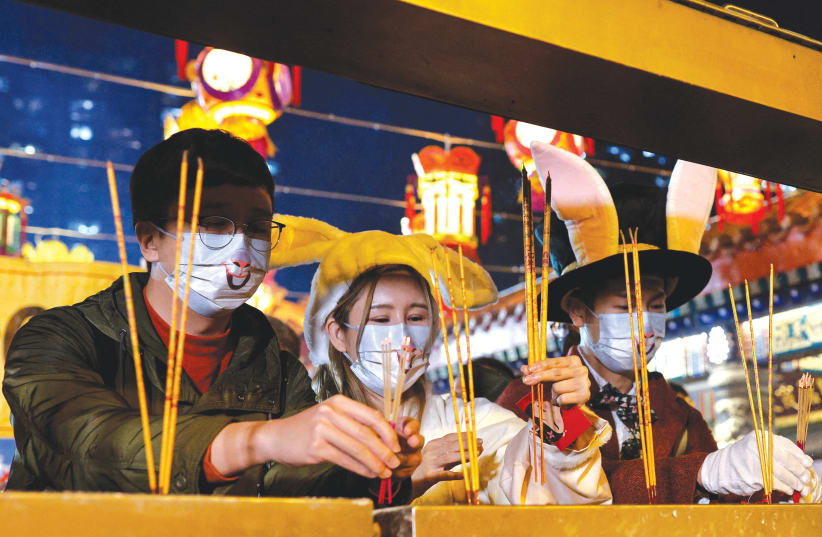 Worshippers wearing facemasks with rabbit faces make offerings of incense sticks at lunar new year (photo credit: TYRONE SIU/ REUTERS)