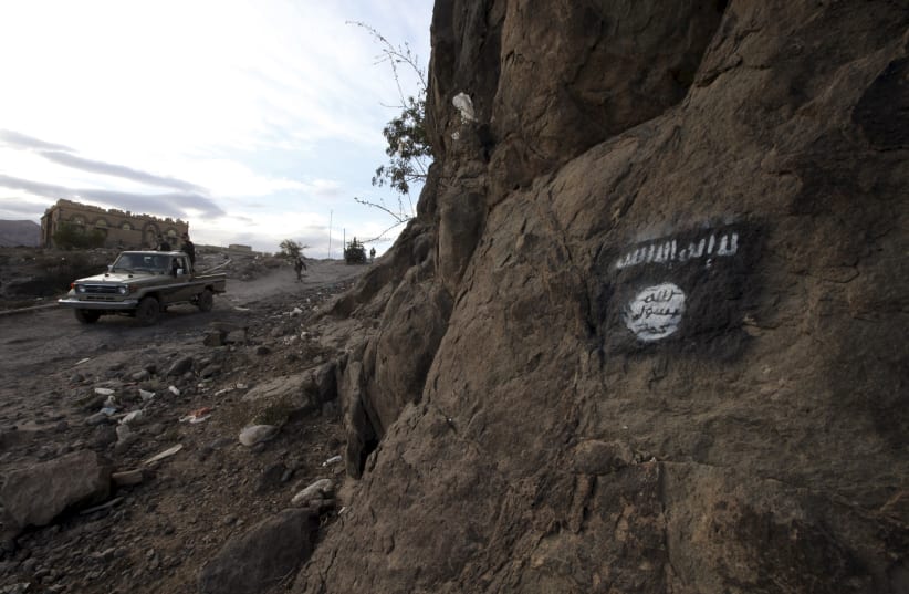  Shi'ite Houthi rebels drive a patrol truck past an Ansar al-Sharia flag painted on the side of a hill, along a road in Almnash, the main stronghold of Ansar al-Sharia, the local wing of Al Qaeda in the Arabian Peninsula (AQAP) in Rada, Yemen November 22, 2014 (photo credit: REUTERS/MOHAMED AL-SAYAGHI)