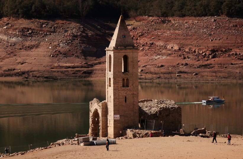  Tourists walk while fishermen collect fish from the Sau reservoir next to the church of the village of San Roman de Sau which was partially submerged and re-emerged as Sau reservoir has the lowest level since 1990 due to extreme drought in Catalonia, near Vic, Spain March 15, 2023. (photo credit: NACHO DOCE/REUTERS)