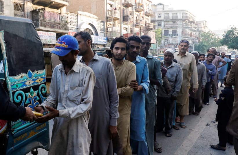 People stand in queue to receive charity food handout, during the fasting month of Ramadan, along a road in Karachi, Pakistan March 30, 2023.  (photo credit: REUTERS/AKHTAR SOOMRO)