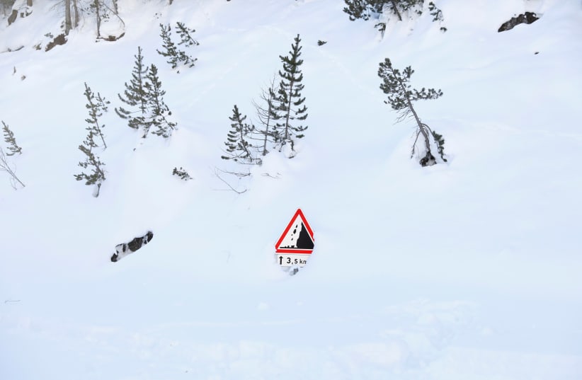  A sign that warns of avalanche dangers protrudes from the snow on a mountain pass where migrants try to cross from Italy into France, near the town of Bardonecchia in northern Italy, December 20, 2017. (photo credit: SIEGFRIED MODOLA/REUTERS)