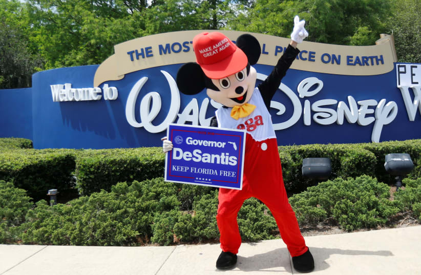 A person wearing a mouse costume dances while holding a Governor Ron DeSantis poster where supporters of Florida's Republican-backed "Don't Say Gay" bill gather for a rally outside Walt Disney World in Orlando, Florida, US April 16, 2022. (photo credit: REUTERS/OCTAVIO JONES)