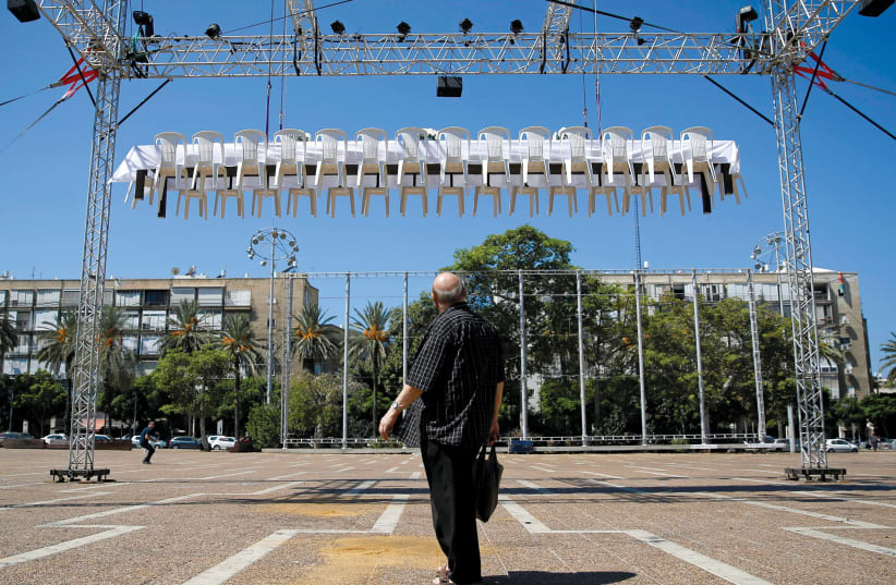  A man looks at a festive table as it is lifted above the ground as part of an installation titled ‘The Unreachable Meal’ organized by Latet, a charity established to help fight poverty in Israel, at Rabin Square in Tel Aviv.  (photo credit: AMIR COHEN/REUTERS)