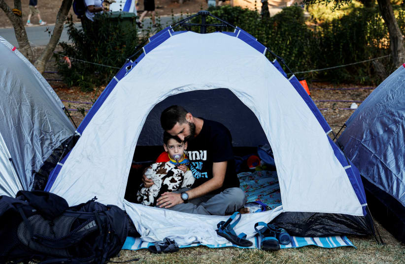  A man cuddles a boy in a tent erected in demonstration against Israeli Prime Minister Benjamin Netanyahu and his nationalist coalition government's judicial overhaul near the Knesset, Israel's parliament in Jerusalem July 24, 2023. (photo credit: REUTERS/AMMAR AWAD)