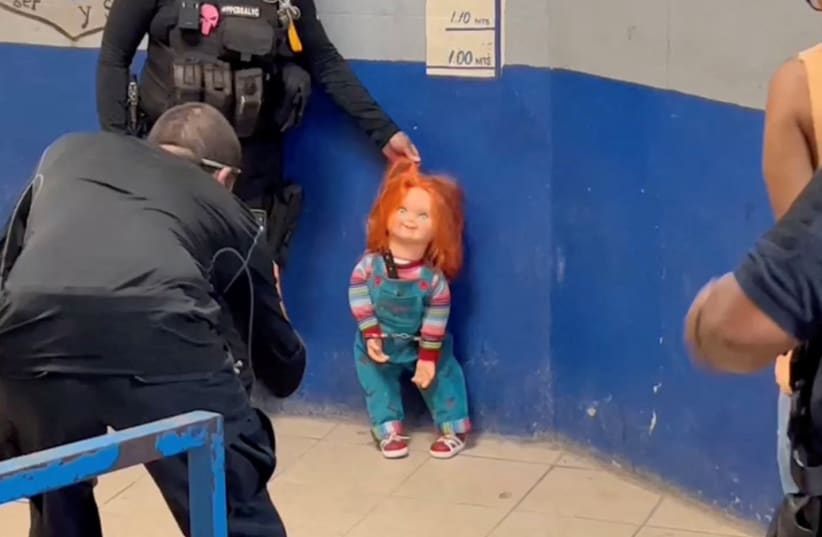 A police officer holds the handcuffed "demon doll" Chucky by its hair after arresting Carlos "N", a man who used the doll with a knife to rob people, according to local media, in Monclova, Mexico, September 11, 2023, in this screen grab obtained from a handout video. (photo credit: Noticias NRT Mexico/Handout via REUTERS)