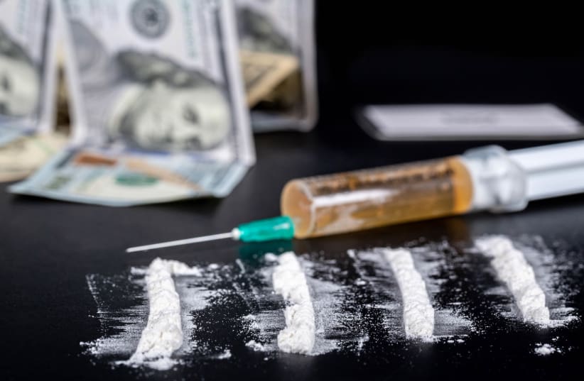  White powder sprinkled on a black background, behind money and a syringe with drugs. (photo credit: FLICKR)