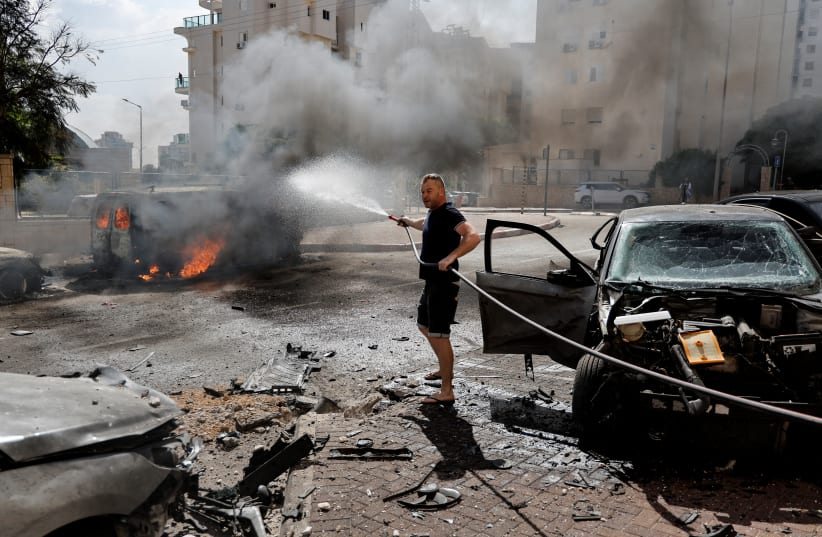  A man works to put out a fire engulfing a van, as rockets are launched from the Gaza Strip, in Ashkelon, southern Israel October 7, 2023. (photo credit: REUTERS/AMMAR AWAD)