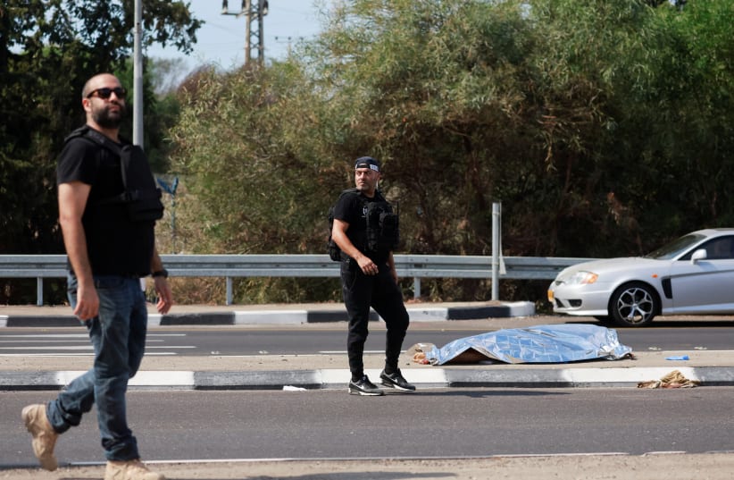 Israeli security personnel walk near the body of a dead man, as Hamas launches a surprise attack from the Gaza Strip, near Ashkelon, southern Israel October 7, 2023.  (photo credit: REUTERS/AMMAR AWAD)