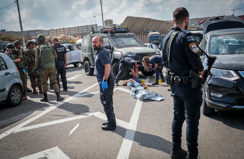 Police and security personnel gather around the body of a Palestinian terrorist at the scene of a shooting attack at "HaMinharot" checkpoint, near Jerusalem, October 11, 2023. (photo credit: NOAM REVKIN FENTON/FLASH90)