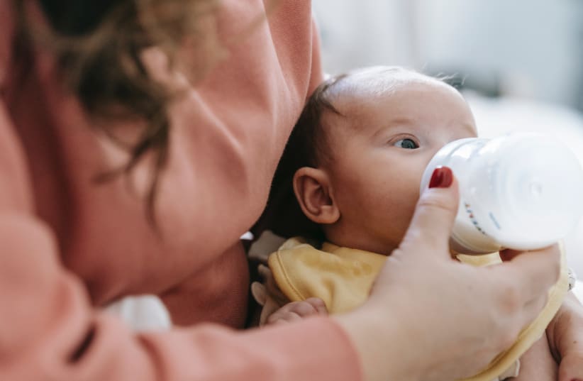  A holds a baby and feeds them milk from a bottle. (photo credit: PEXELS)