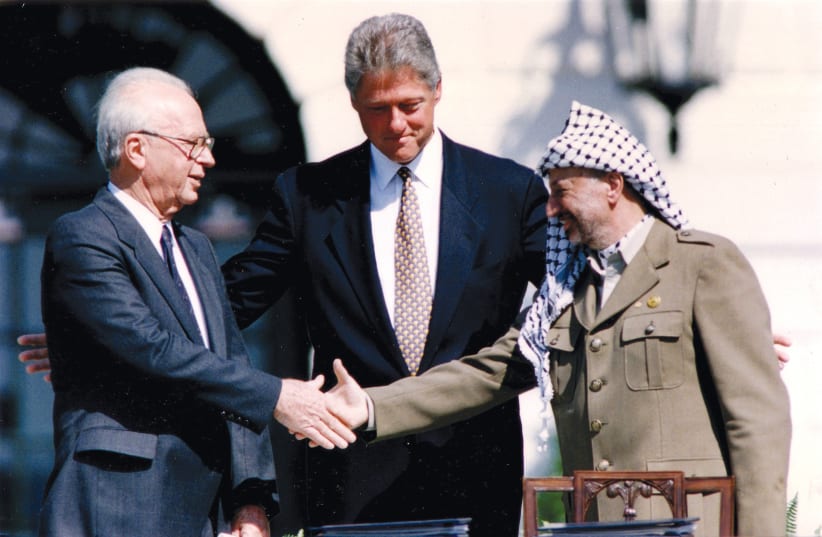  PLO chairman Yasser Arafat shakes hands with Israeli prime minister Yitzhak Rabin as US president Bill Clinton stands between them, after the signing of the Oslo Peace Accords at the White House on September 13, 1993. (photo credit: GARY HERSHORN/REUTERS)