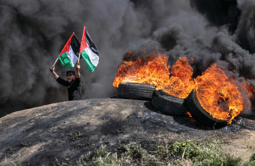  THEN, AS now: Waving Palestinian flags amid fumes from flaming tires east of Gaza City, in April.  (photo credit: MAHMUD HAMS/AFP via Getty Images)