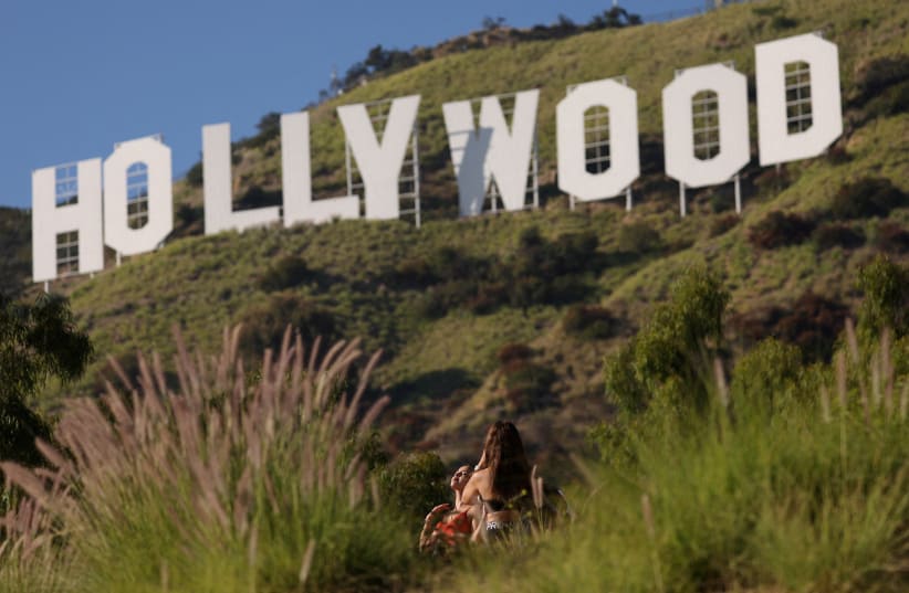 A woman poses by the iconic Hollywood sign on the day members of the Writers Guild of America (WGA) approved a new three-year contract with major studios, in Los Angeles, California, U.S., October 9, 2023. (photo credit: MARIO ANZUONI/REUTERS)
